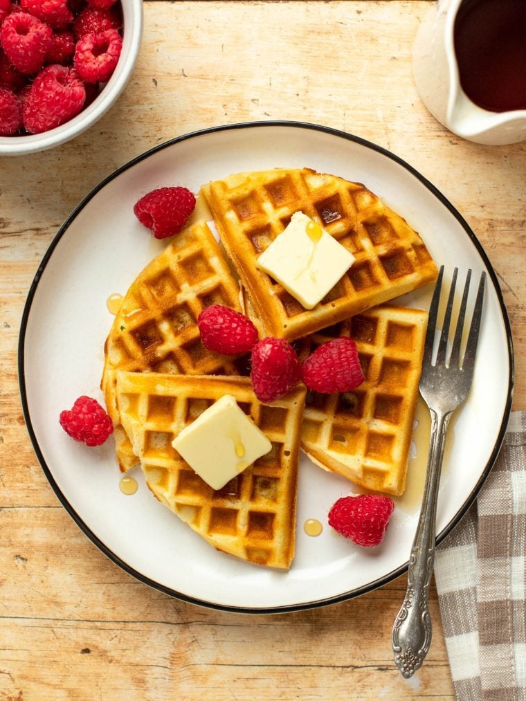 Plate of waffles topped with butter, syrup, and raspberries.