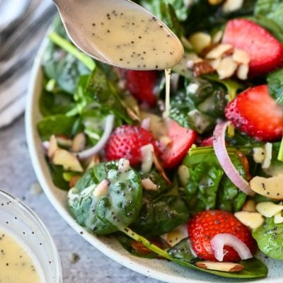 Spoon drizzling poppy seed dressing onto a salad.