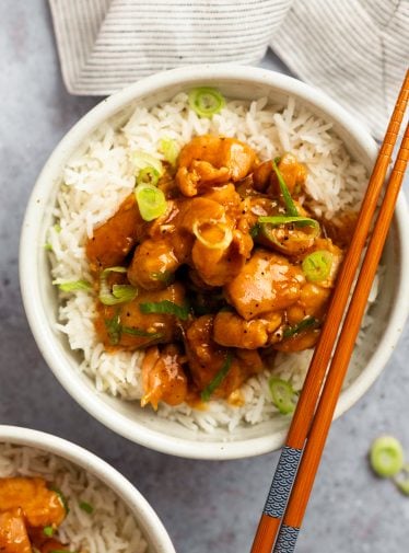 Chopsticks on a bowl of bourbon chicken over rice.
