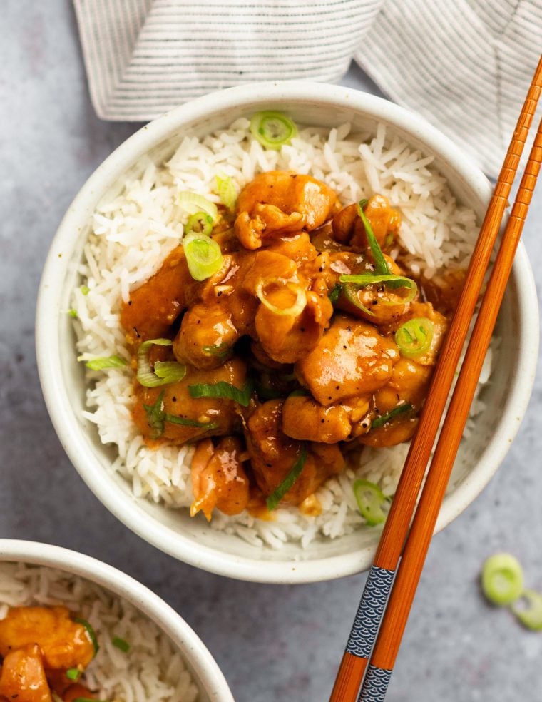 Chopsticks on a bowl of bourbon chicken over rice.