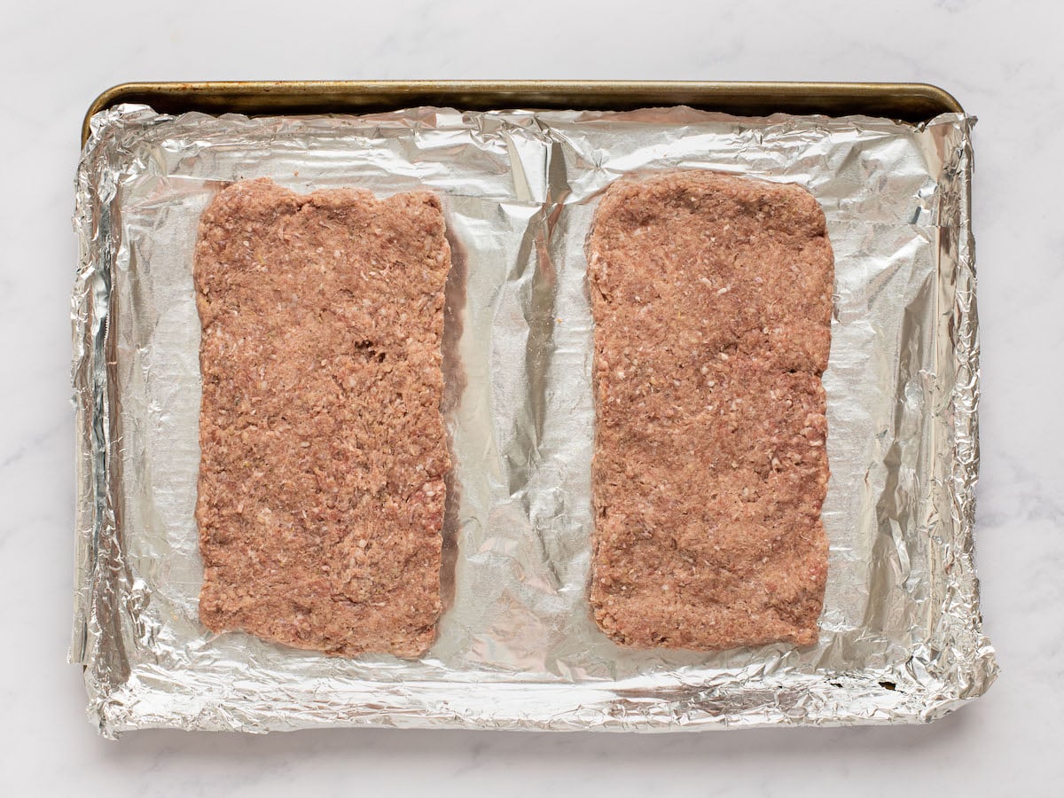 Meat shaped into 2 loaves on a baking tray.