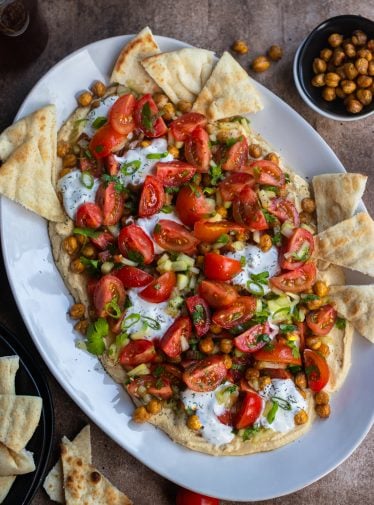 Hummus board with pita, tomatoes, and more.