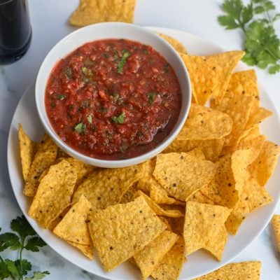 Bowl of salsa on a plate with chips.