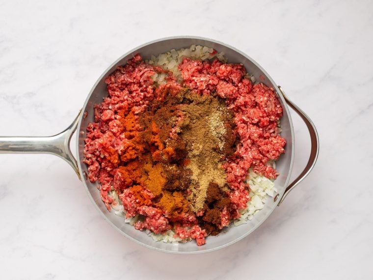 adding the beef and spices to the skillet with the onions and garlic