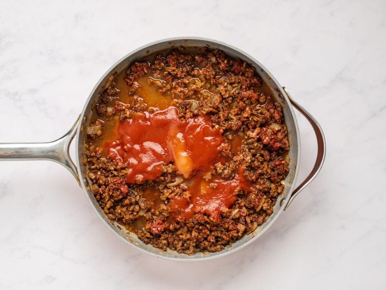 Adding the tomato sauce, water, sugar, and lime juice to the beef in the skillet
