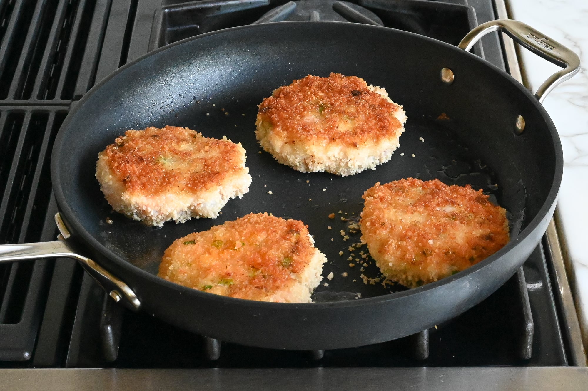 Shrimp burgers in the skillet browning on the second side.