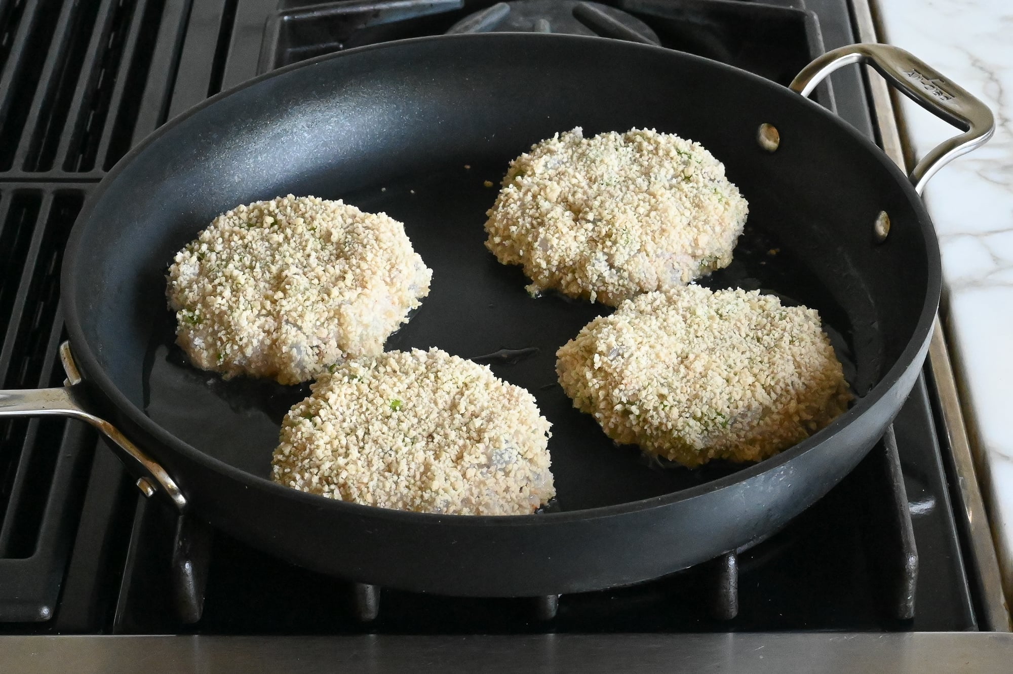 Shrimp burgers in the skillet browning on the first side.
