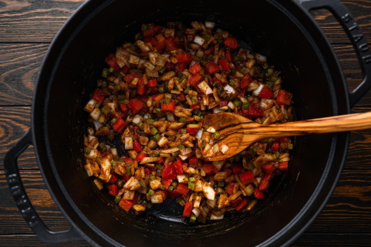 onion, celery, and bell pepper being stirred with roux in dutch oven