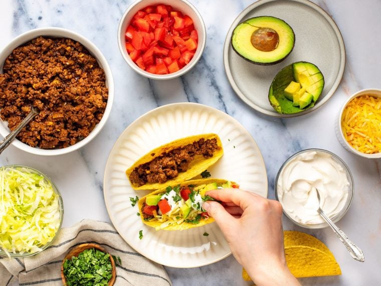Person adding toppings to a taco on a plate.