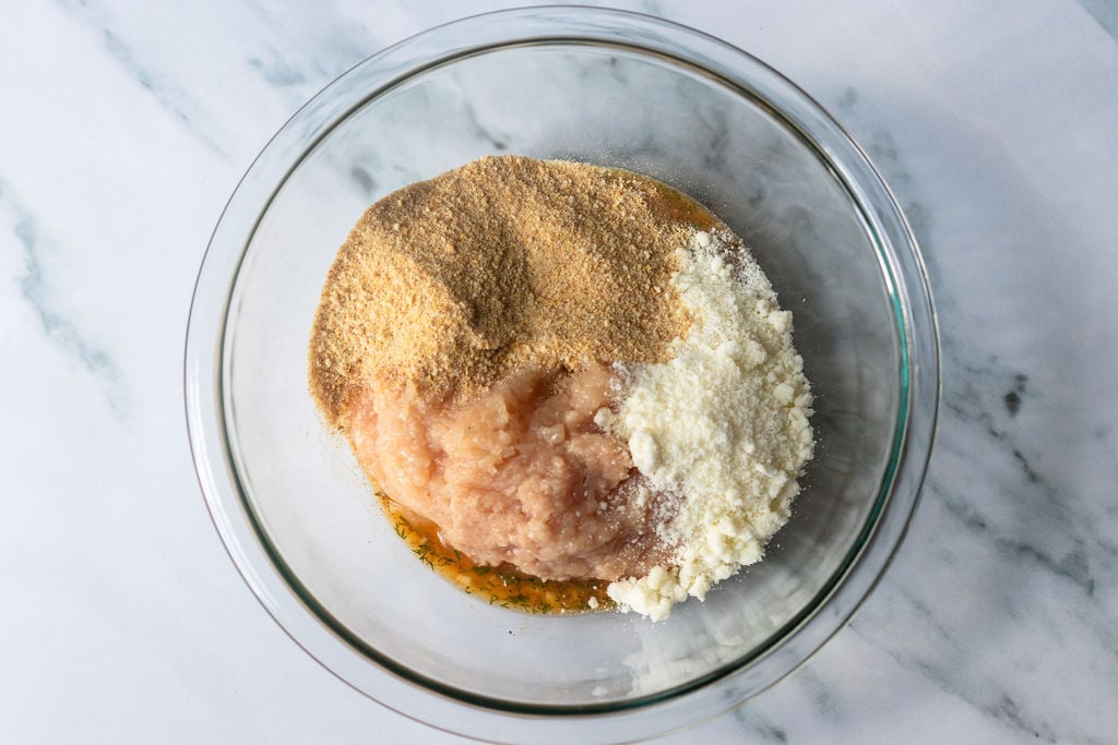 Ground chicken, grated cheese, and breadcrumbs in a glass bowl.