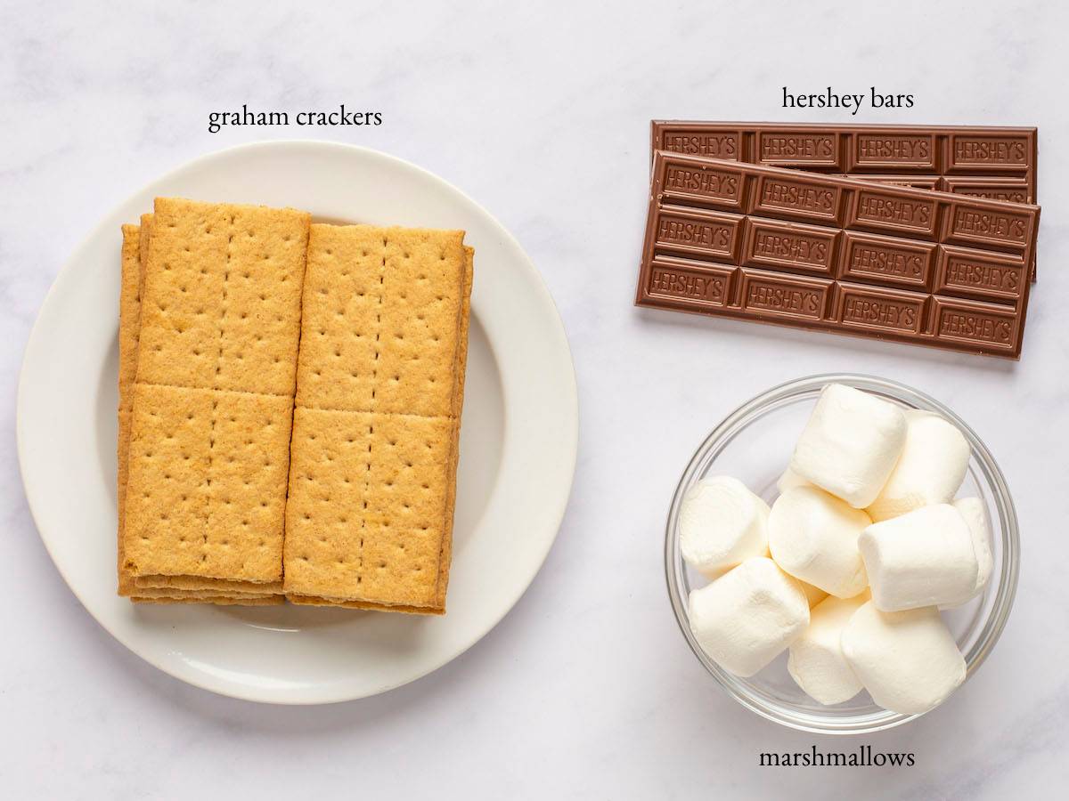 S'mores ingredients - graham crackers, Hershey bars, and marshmallows - on a marbled surface.