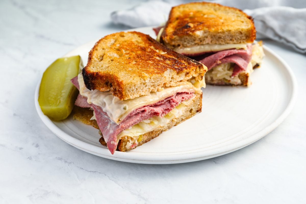 Halved reuben sandwich on a white plate.