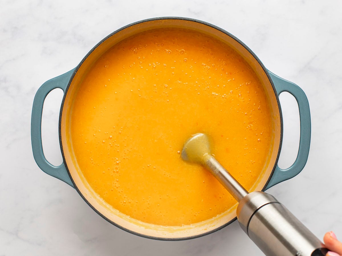 Immersion blender in a pot of orange soup.