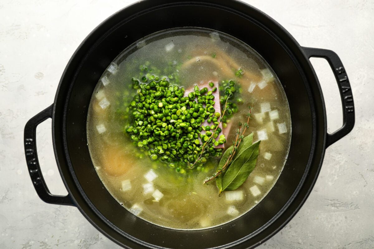Chicken broth, water, ham steak, bacon, peas, thyme sprigs, and bay leaves added to the pot.