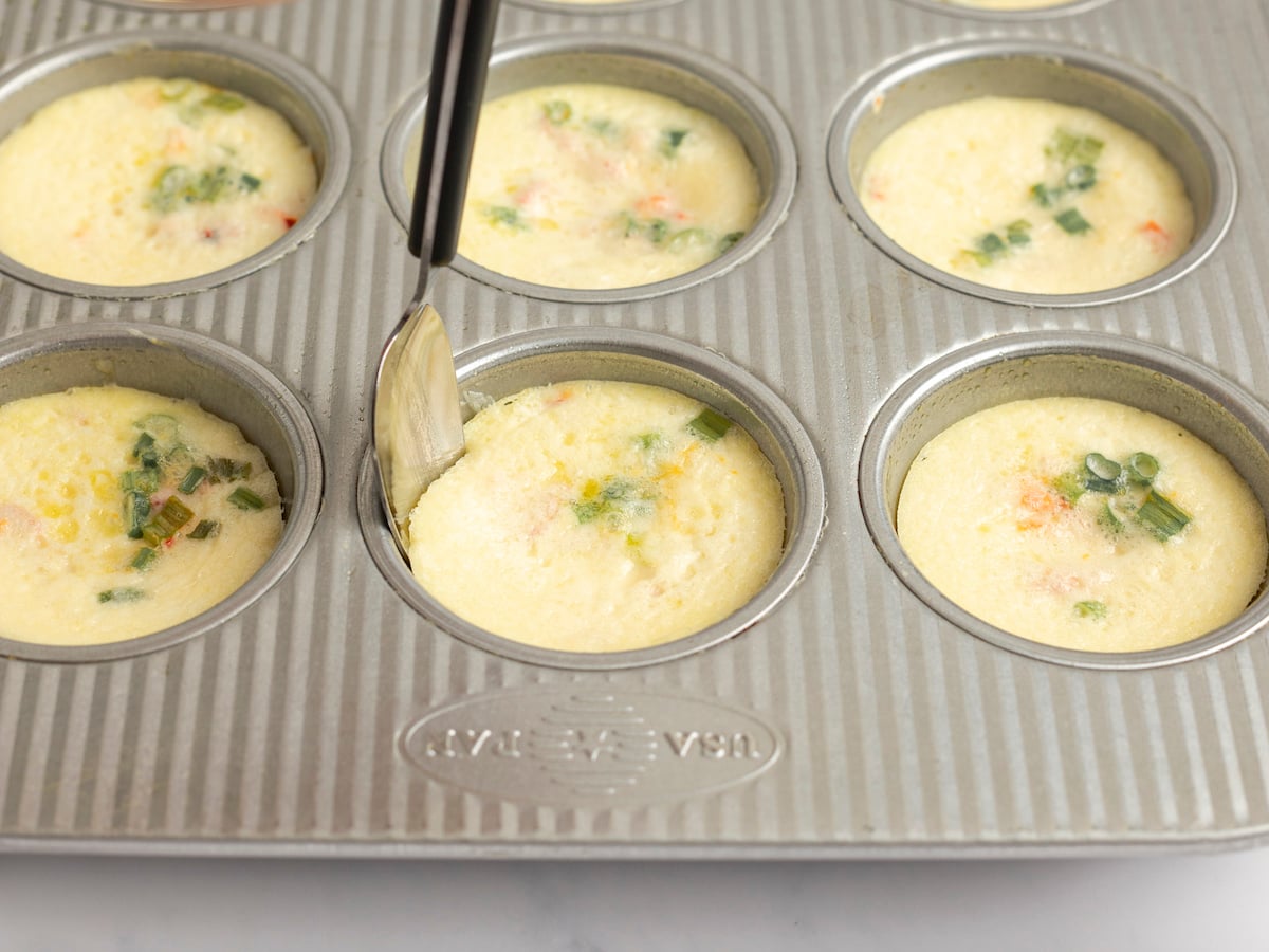 small spoon loosening egg bites from edges of pan
