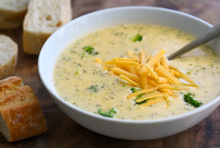 broccoli cheddar soup in bowl on cutting board with sliced baguette