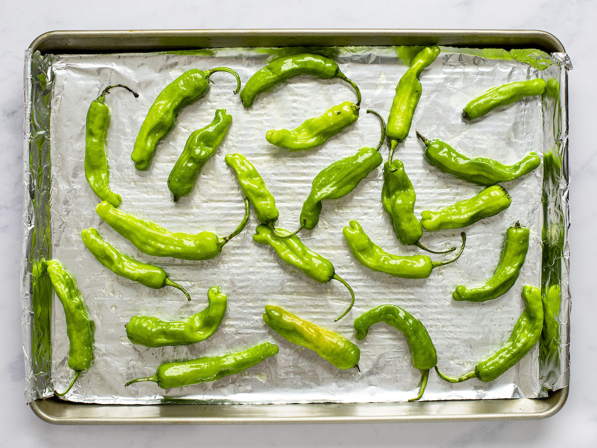 shishito peppers evenly spaced on foil-lined baking sheet tossed with oil and salt