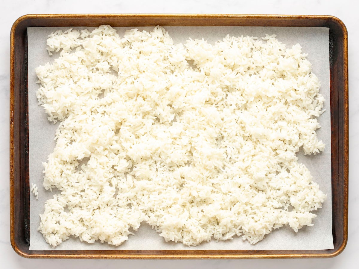 foil-lined baking sheet with cooked rice spread on it.
