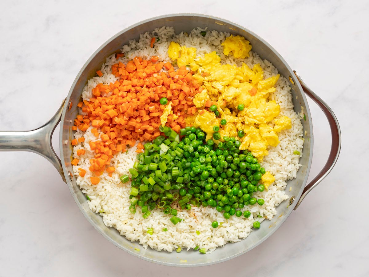 peas, egg and carrot mixture, dark green scallions, soy sauce, and sesame oil added to rice in skillet.
