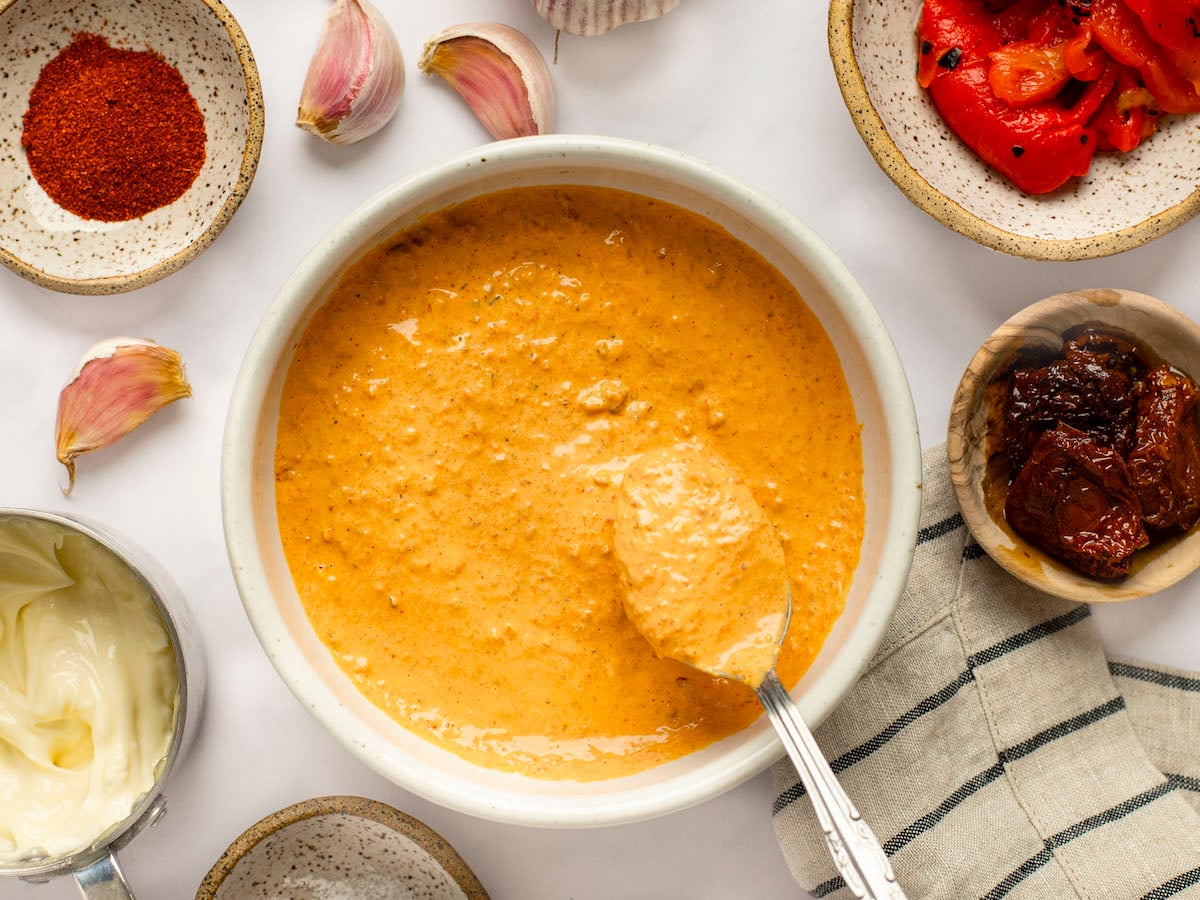 Sun-dried tomato and red pepper aioli in a bowl with ingredients surrounding it.