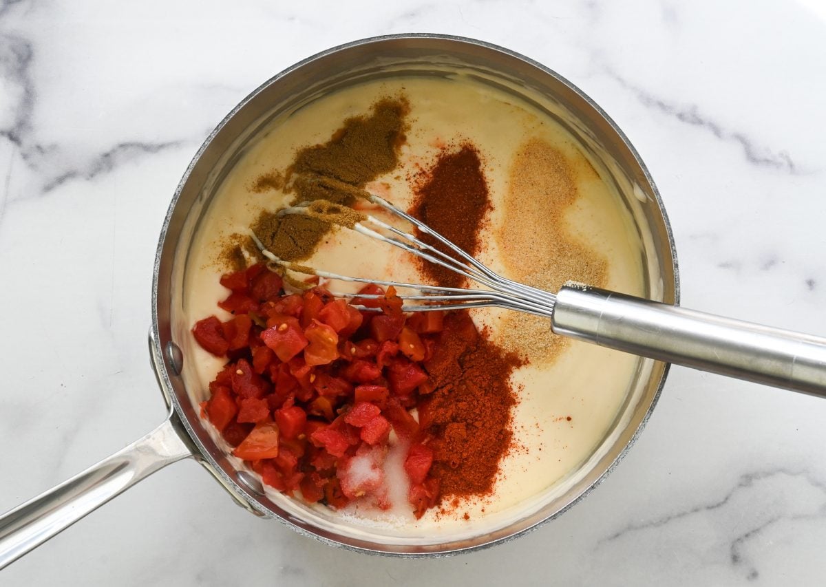 Stirring in the salt, chili powder, cayenne pepper, cumin, garlic powder, onion powder, and diced tomatoes and green chilies.
