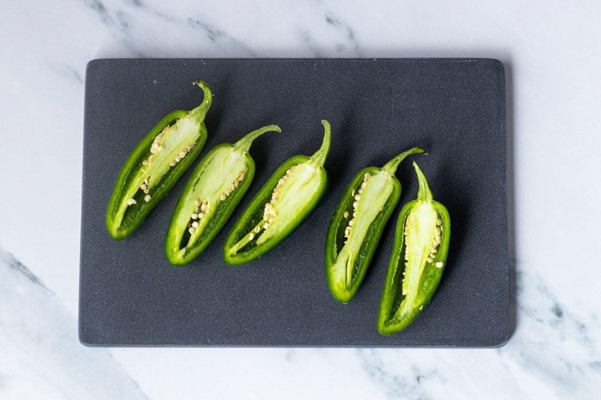 jalapeños cut in half lengthwise on a cutting board