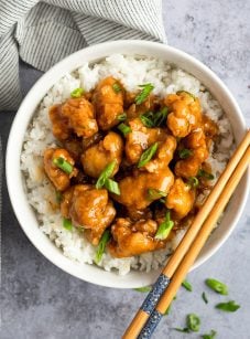 orange chicken in bowl with rice and chopsticks