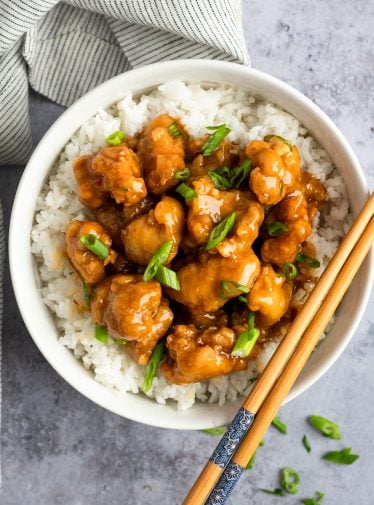 orange chicken in bowl with rice and chopsticks