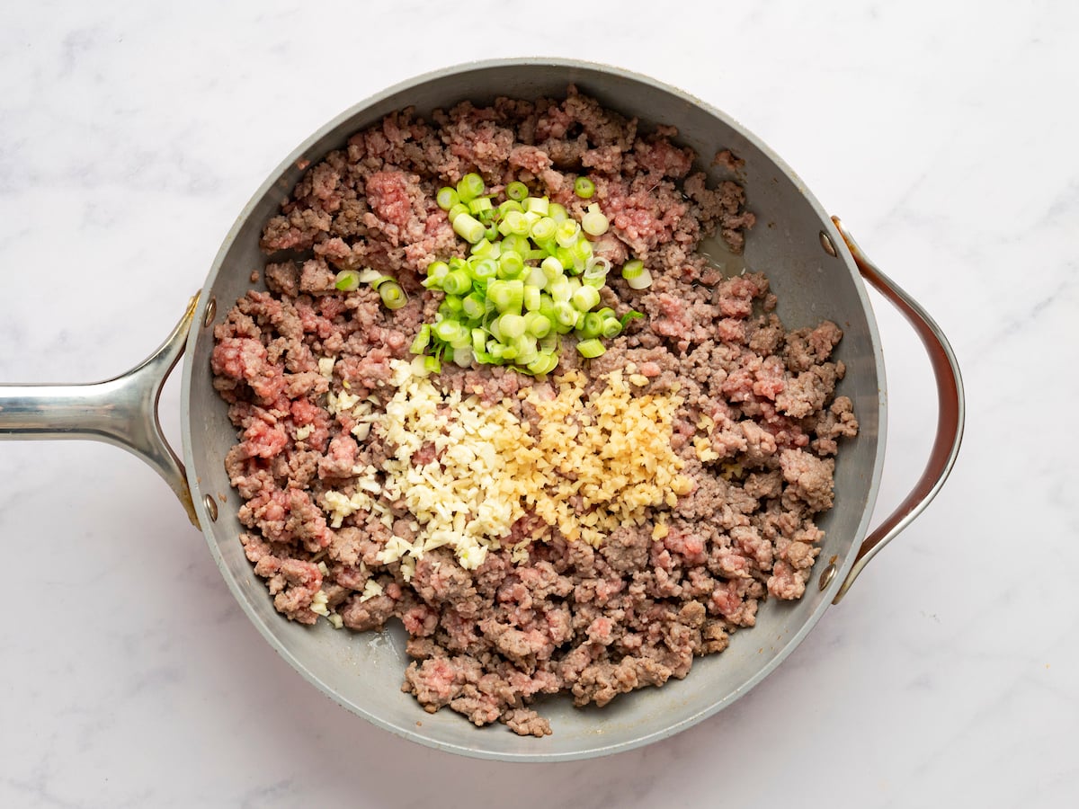 adding garlic, ginger, and scallions to beef in skillet.