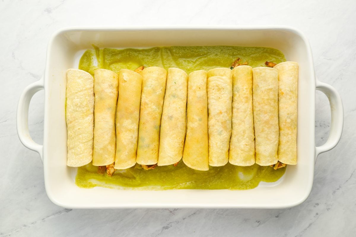 rolled chicken enchiladas arranged in baking dish.
