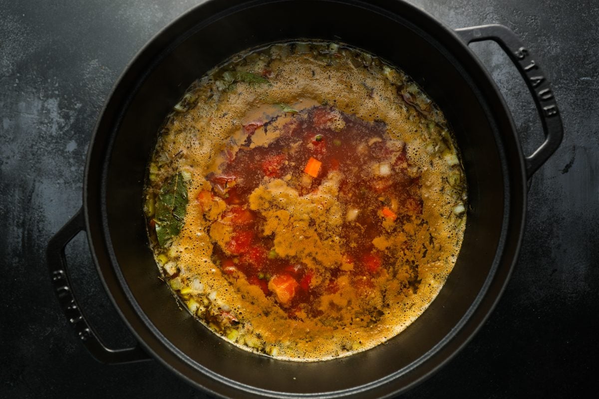 simmering broth with vegetables, tomatoes, and bacon in pot.