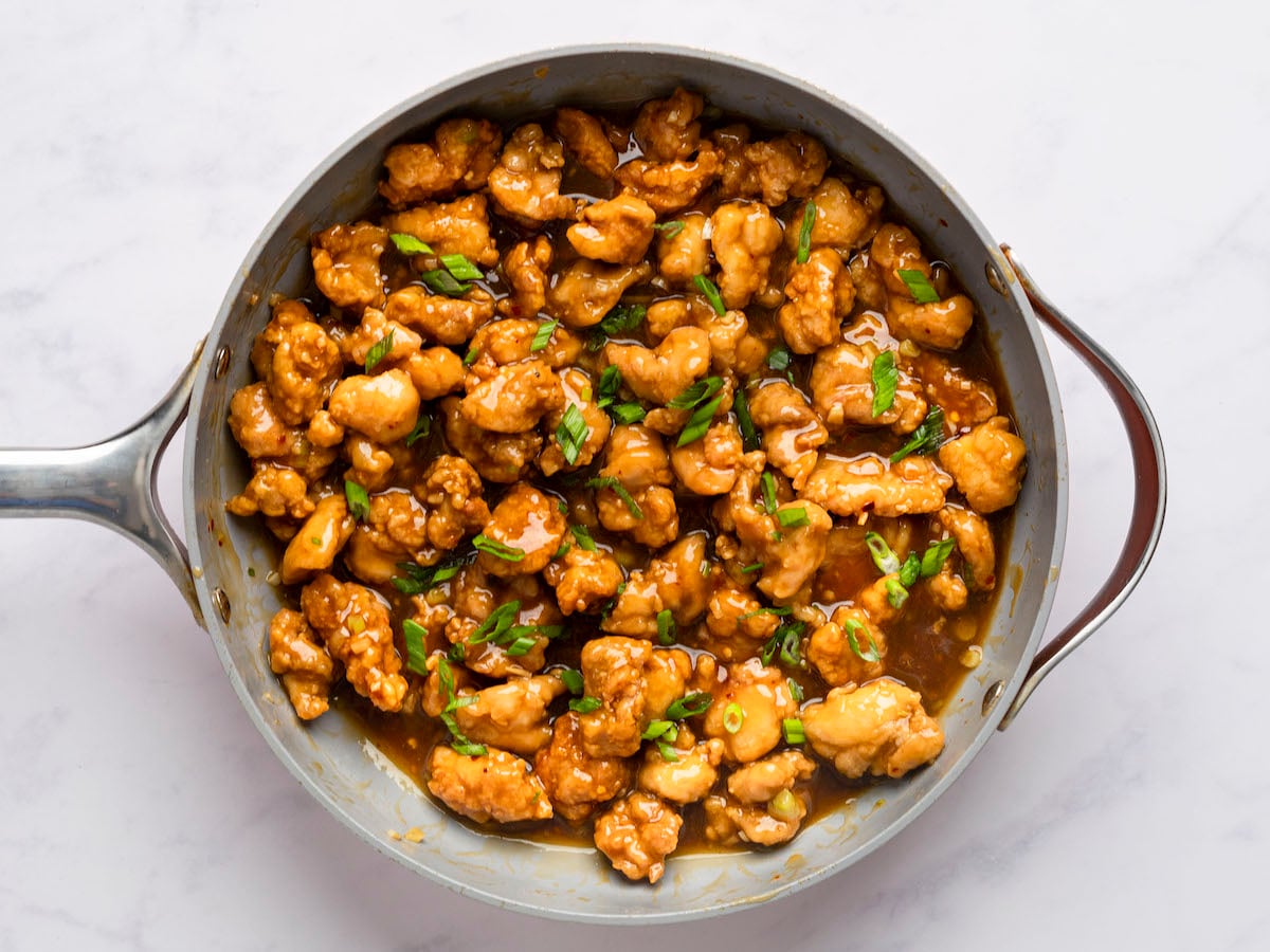 cooked orange chicken with scallion garnish in skillet