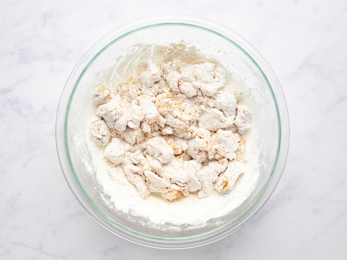 coating marinated chicken with cornstarch and flour mixture in bowl.