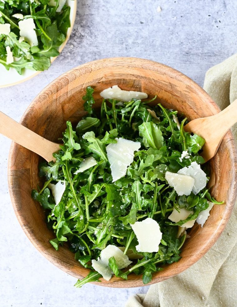arugula salad in wooden bowl with wooden spoons.