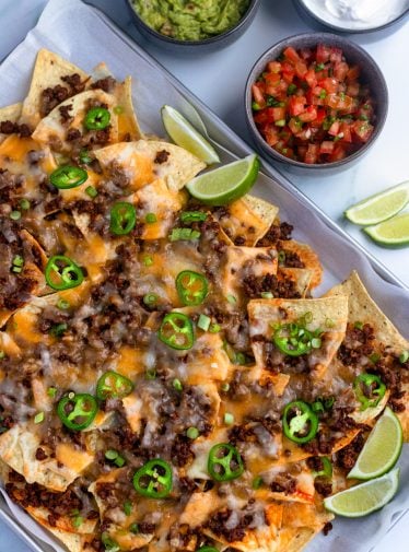 beef nachos on sheet pan with salsa, guacamole, and sour cream.