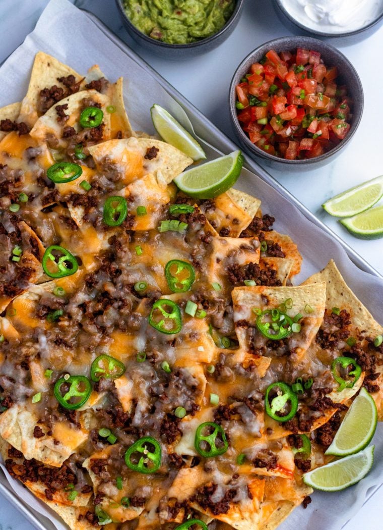 beef nachos on sheet pan with salsa, guacamole, and sour cream.