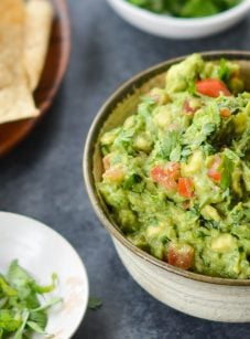 A bowl of guacamole with chips on a table.