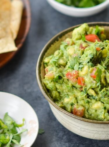 A bowl of guacamole with chips on a table.