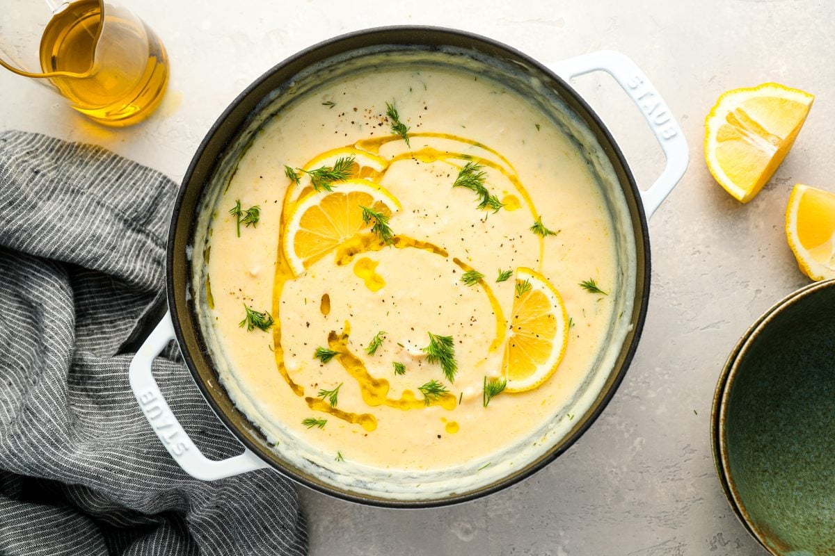 Avgolemono soup in Dutch oven with gray striped dish towel.