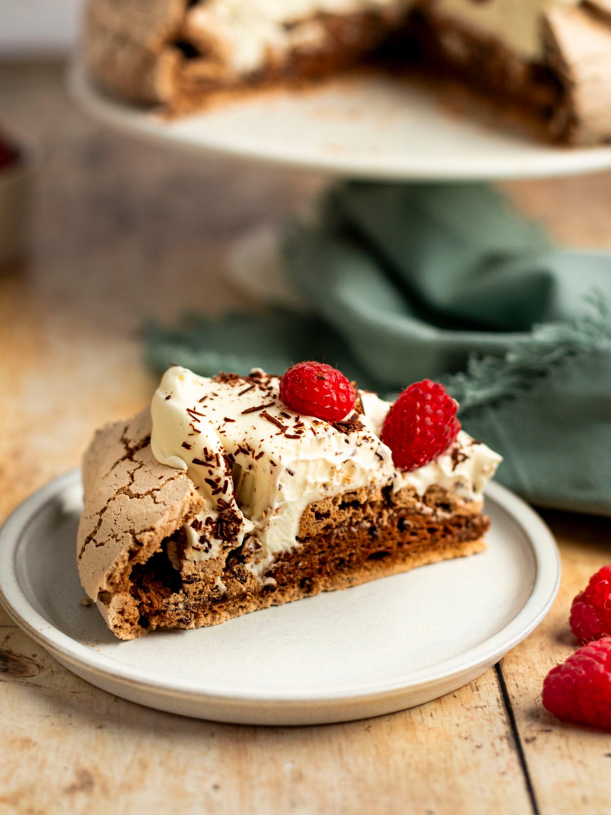 slice of chocolate pavlova with whole pavlova in background.