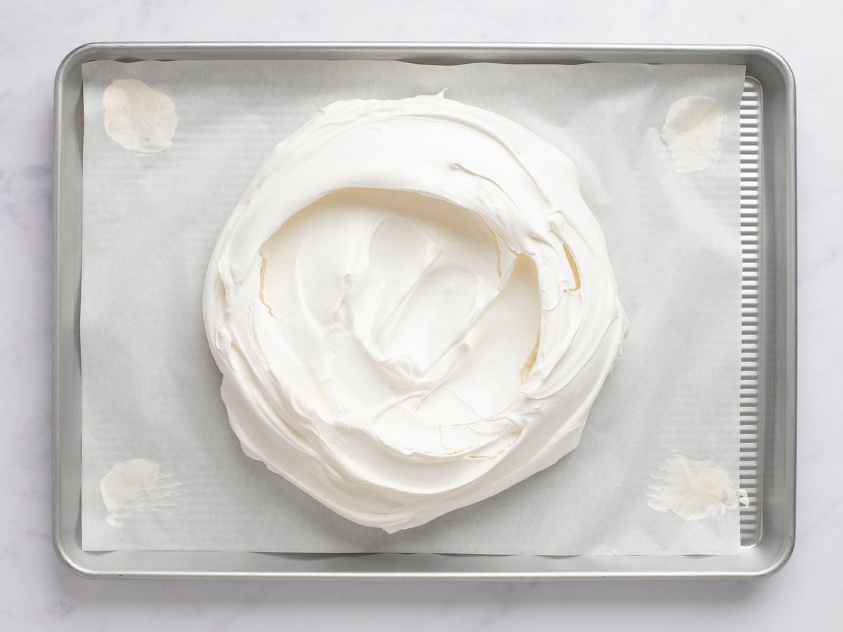 Meringue portion of pavlova on parchment-lined baking sheet with center slightly indented.