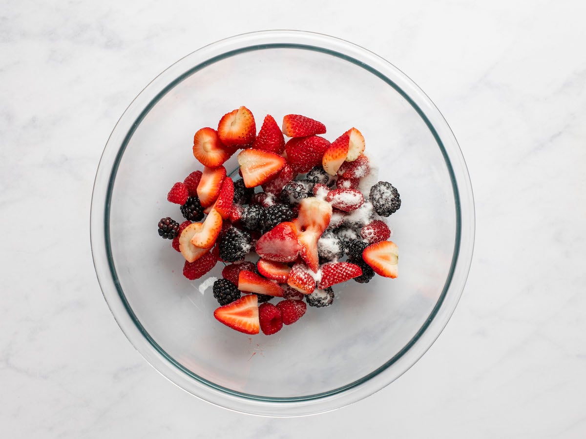 Mixed berries in medium bowl topped with lemon juice and sugar.