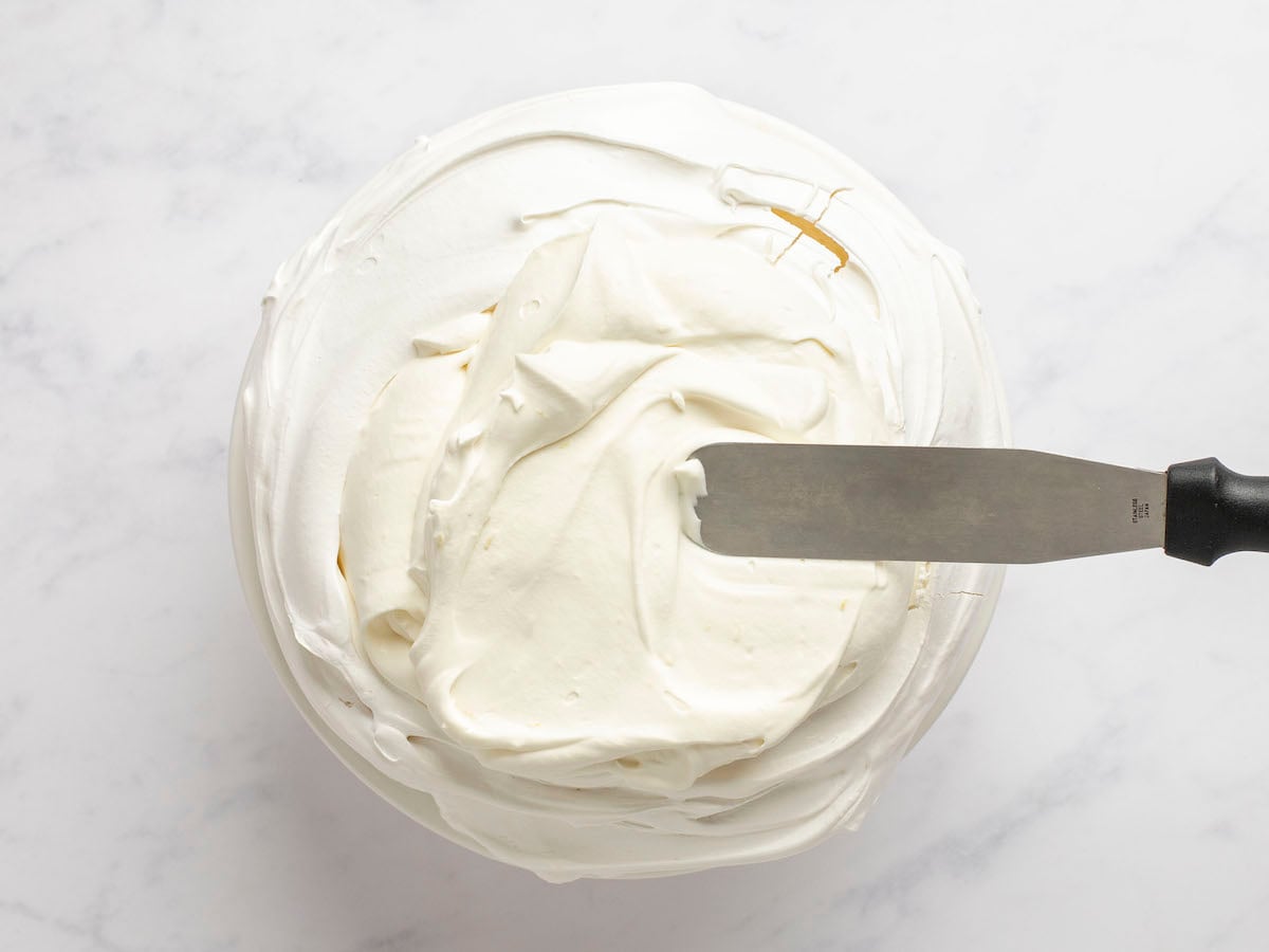 Spatula spreading whipped mascarpone cream onto meringue.