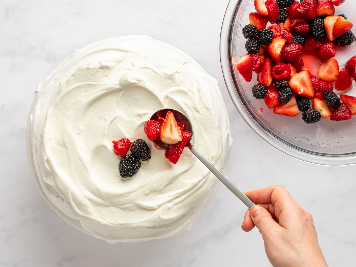 Spooning berry mixture over top the classic pavlova.