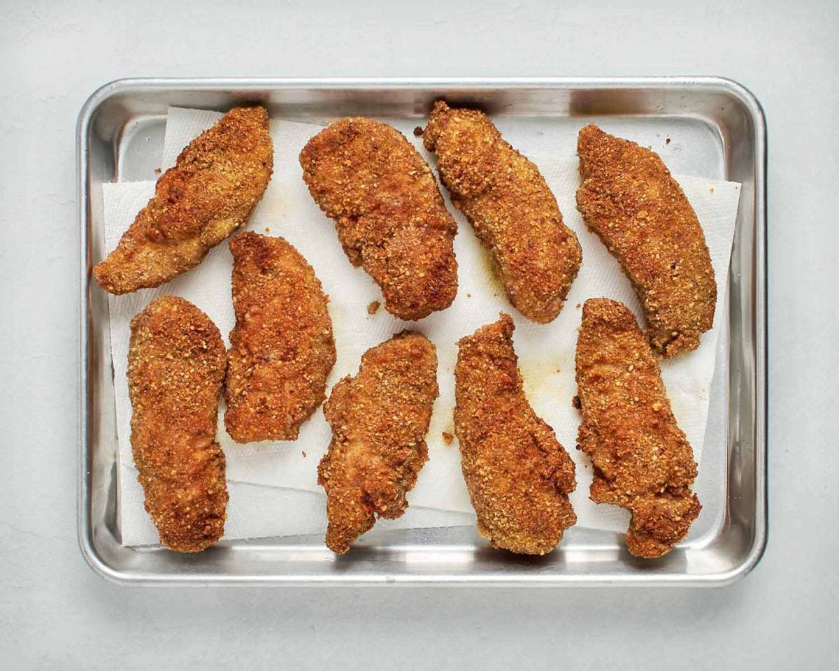 pan-fried pecan crusted chicken tenders on lined baking sheet.