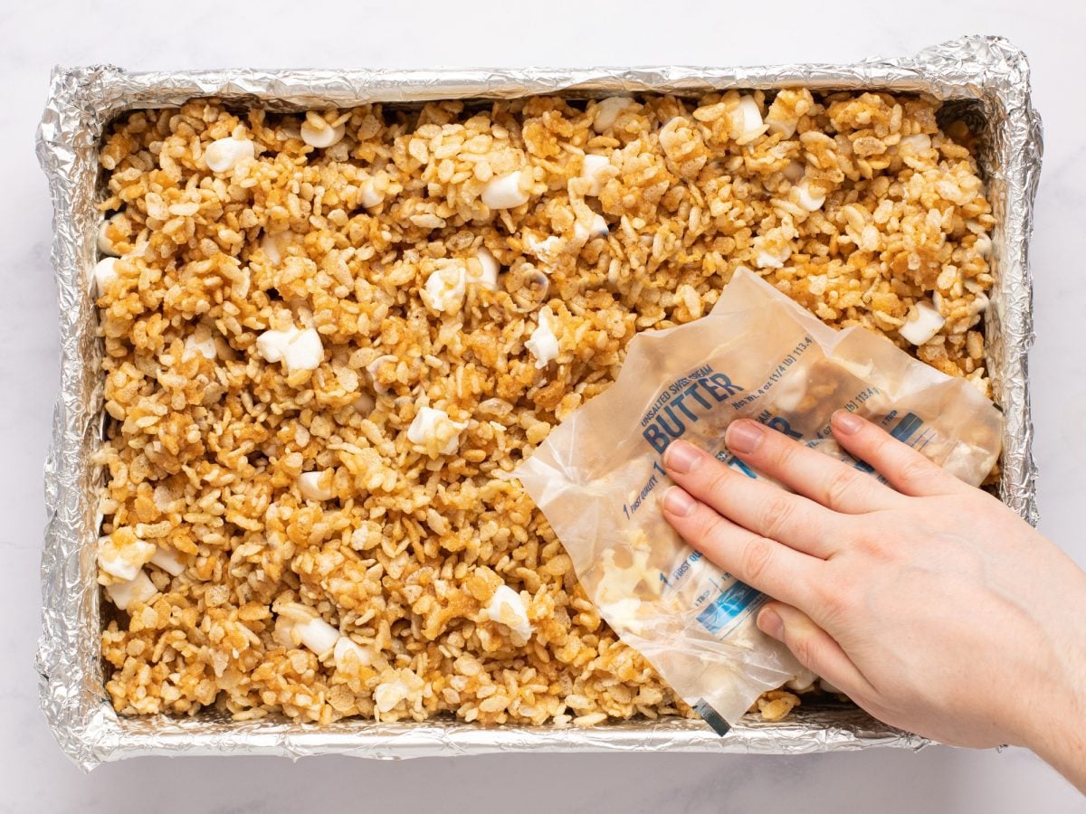 pressing peanut butter rice krispies treats in pan with butter wrapper