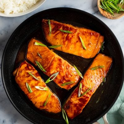 teriyaki salmon in skillet with bowl of white rice and scallions.