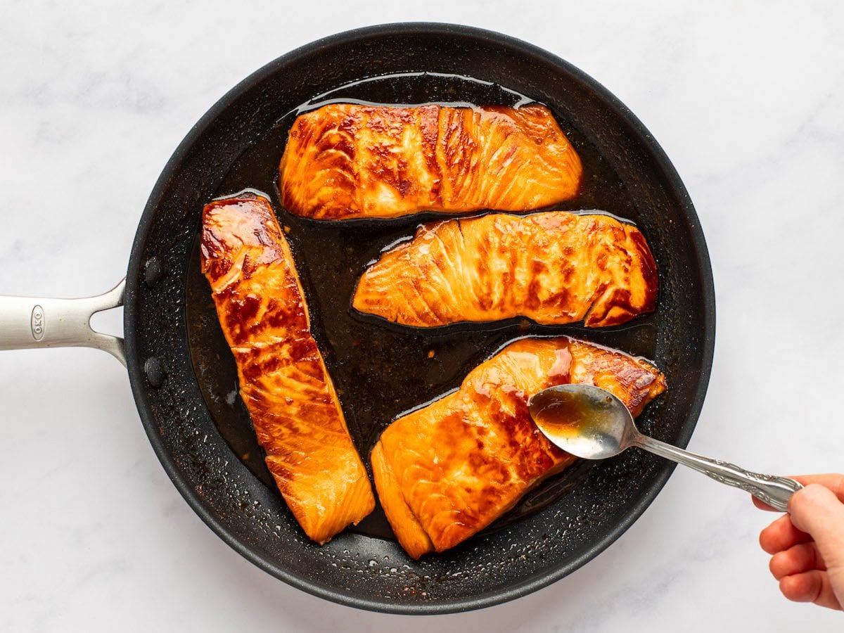 spooning teriyaki sauce over salmon.