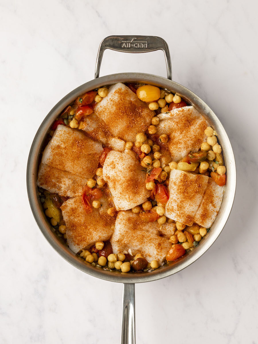 salt and paprika sprinkled overtop the cod in the large pan with tomato chickpea mixture
