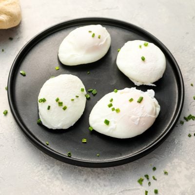 4 poached eggs on a black plate topped with chopped chives